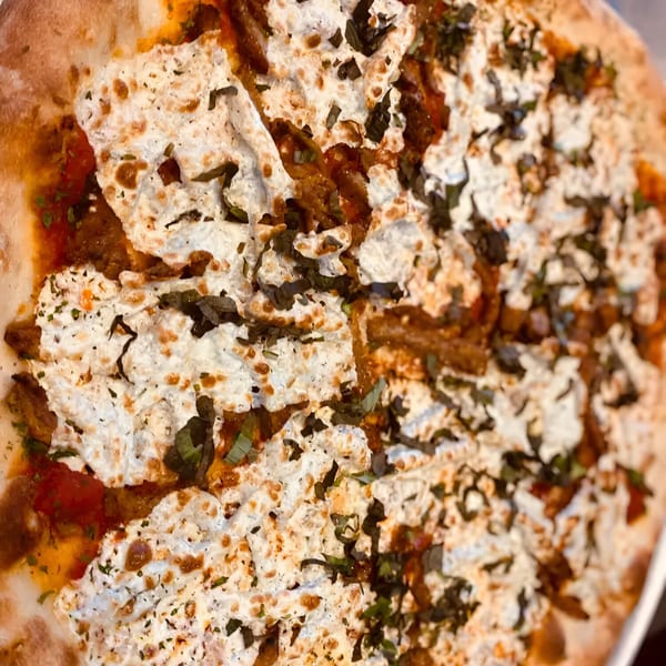 Close-up of a Biaggio Pizzeria pizza with ricotta cheese, tomato sauce, and basil.