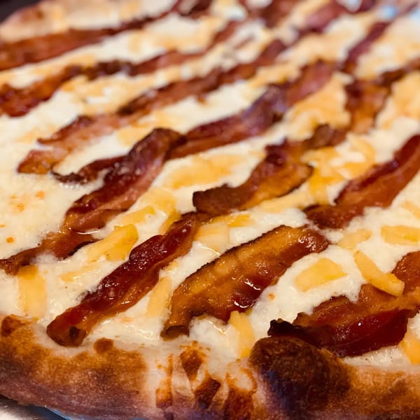 Close-up of a Biaggio Pizzeria pizza with a white sauce base, bacon strips, and cheese.